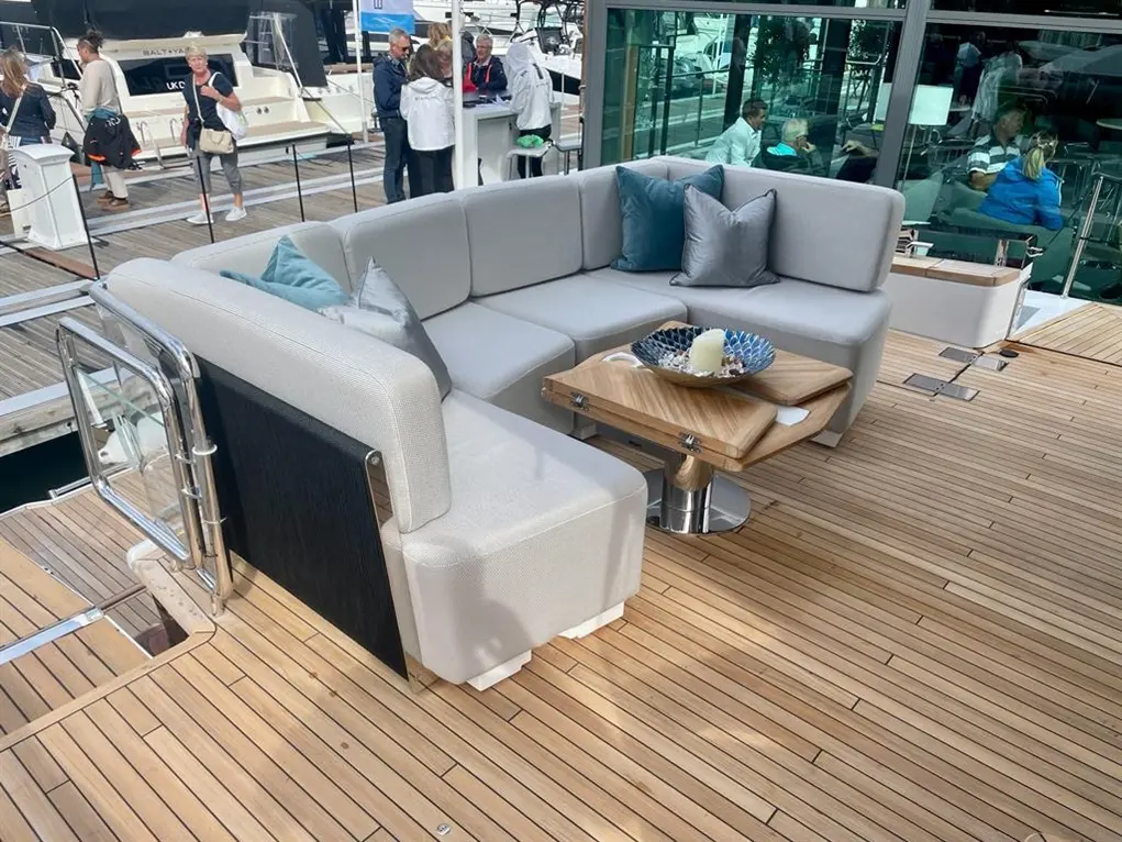 A stylish outdoor seating area on a boat features a curved grey sofa with cushions, a wooden table, and a decorative bowl.